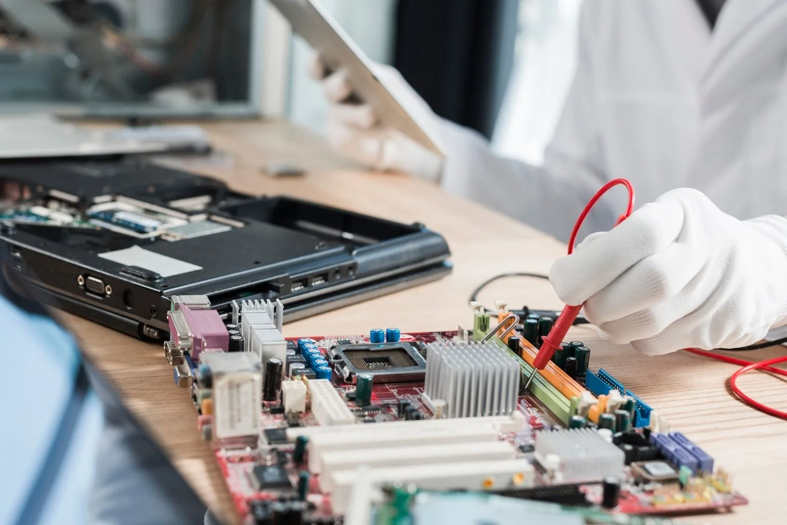Technician repairing a laptop at a repair bench with test leads attached