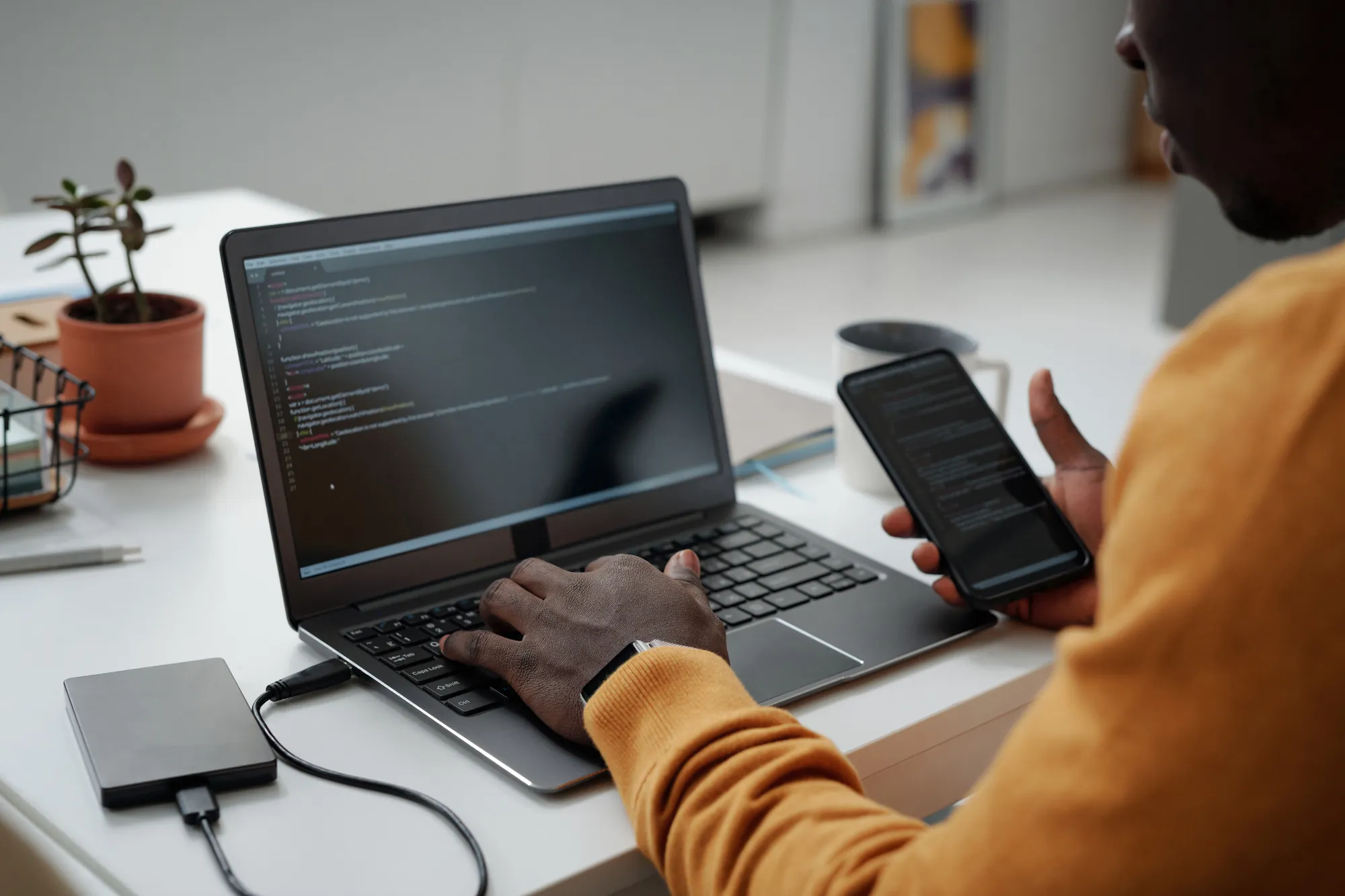 Person using a laptop and phone with an external hard drive connected for data recovery