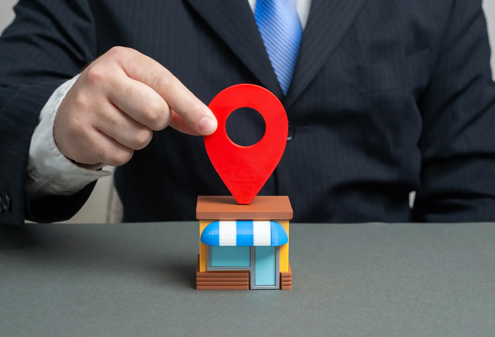 Hand placing a red map pin on a small storefront model to show local search visibility