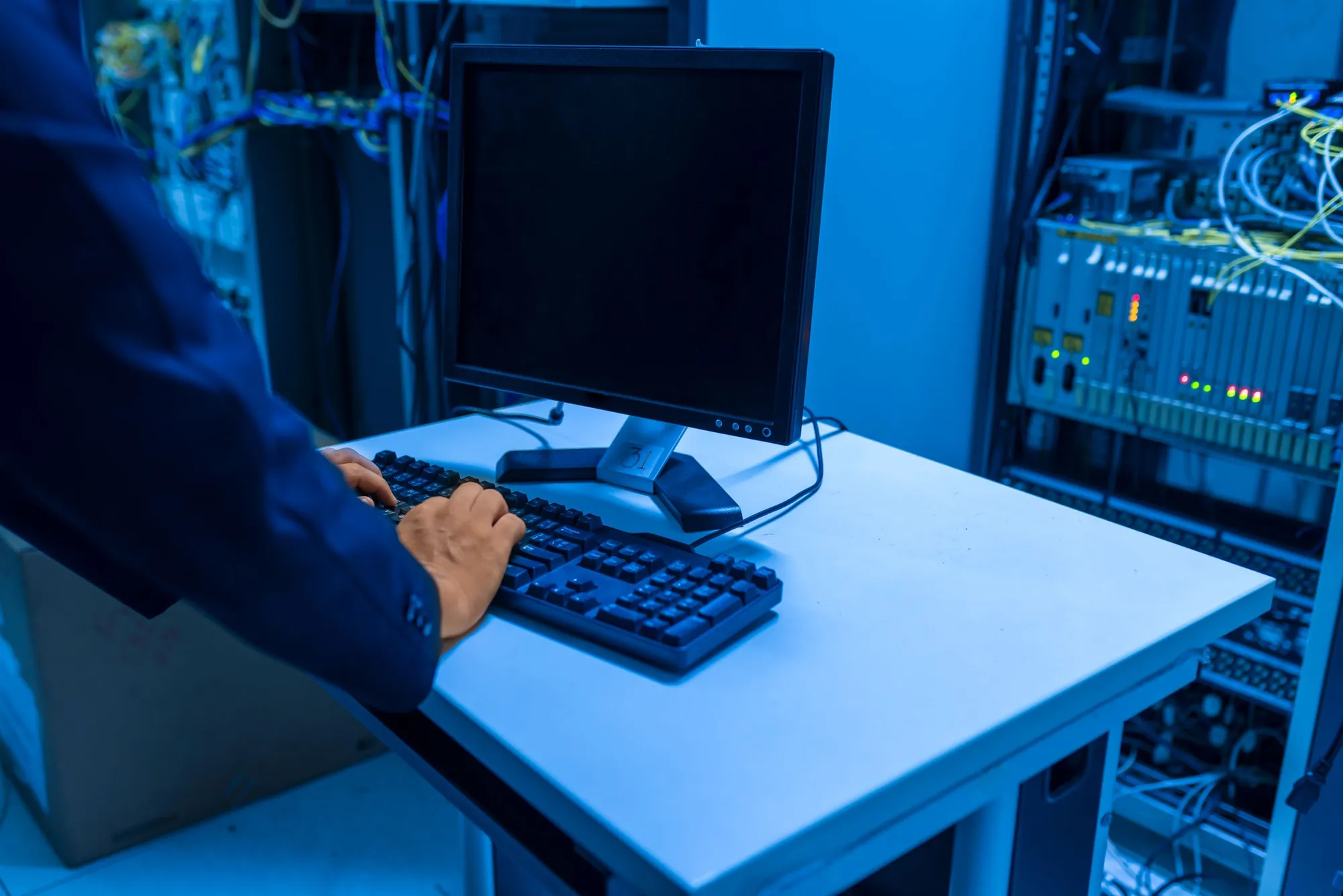 IT technician working at a computer next to a server rack in a network room