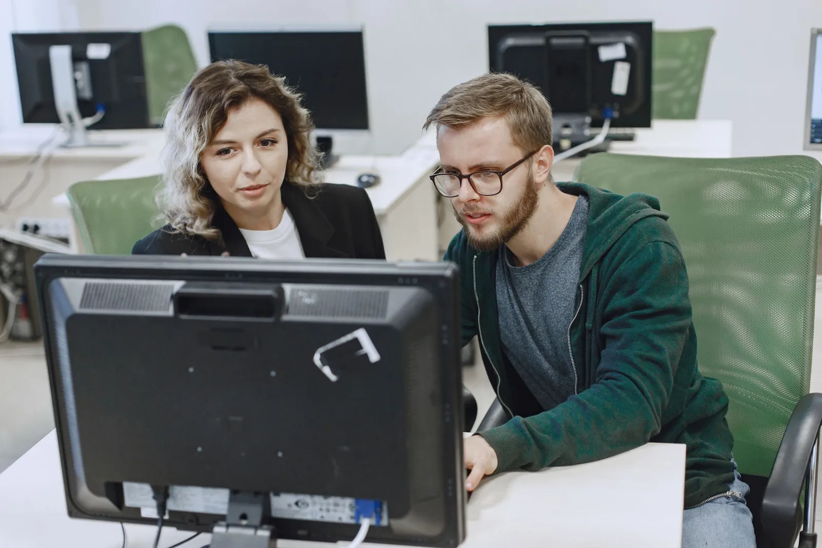 Colleague helping a coworker at her computer in a bright office
